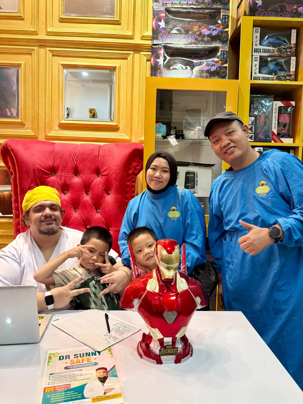 Keluarga pasien memakai gown VIP berfoto bersama dokter dan patung Iron Man